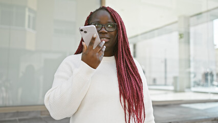 Poster - African american woman with braids using a smartphone on a city street