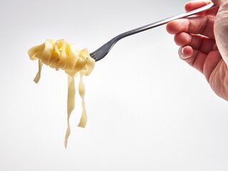 Wall Mural - Close-up of a hand twirling fettuccine pasta on a fork against a white background, suggesting a meal.