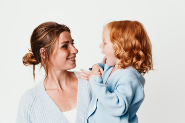 Wall Mural - Happy mother and daughter in matching sweaters smiling at each other on white background