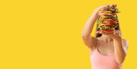 Wall Mural - Beautiful young woman holding stack of many sandwiches on yellow background with space for text