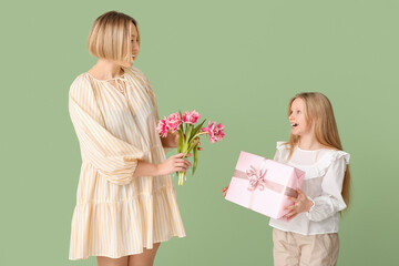 Poster - Beautiful young woman holding bouquet of tulips and her cute little daughter with gift box on green background