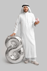 Canvas Print - Young Arab man with balloon in shape of figure 8 and gift box on grey background. International Women's Day