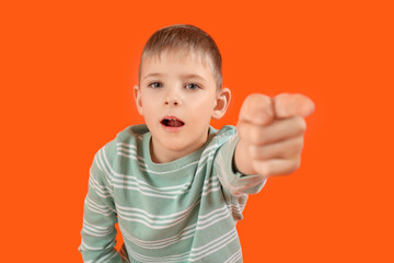 Wall Mural - Shocked little boy pointing at viewer on orange background