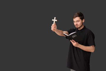 Canvas Print - Religious young man with cross reading Holy Bible on black background