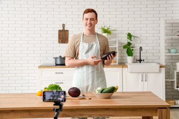 Poster - Young man with fresh vegetables recording cooking video in kitchen