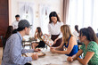 © Kawee - Asian waitress serving food to group of diverse customer in restaurant.