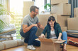 © NonVig/peopleimages.com - Moving, love and couple with boxes in new home unpacking together in living room with happiness. Mortgage, bonding and mature man and woman with cardboard packages at house for property investment.
