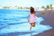 © vvvita - Happy little girl in a pink dress runs along the beach back to the camera in summer