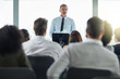© NonVig/peopleimages.com - Podium, mature man and advise in seminar, speaker and audience in event, training and presentation in boardroom. Workshop, speech and talking in conference, entrepreneurship and masterclass for group
