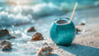 © SashaMagic - Blue coconut with a straw on a sandy beach by the ocean waves.