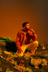 Wall Mural - A man kneels in a pile of plastic waste, his expression contemplative.