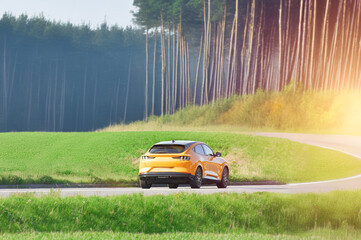 Orange EV SUV Driving Through Green Fields and Forest