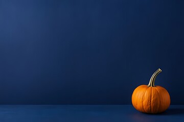 Small orange pumpkin on dark blue surface against empty indigo wall. Minimalist composition with ample copy space. Autumn decoration. Halloween and Thanksgiving concept