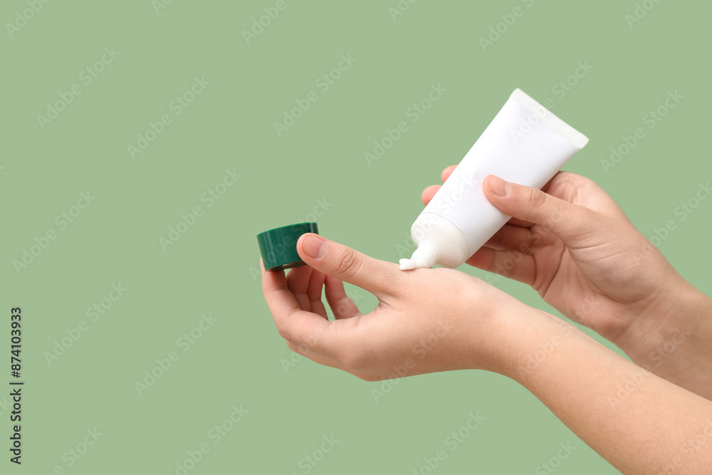 Woman applying cosmetic cream on green background