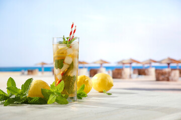 Sticker - Image of copy space for drinks and food and products. Glass of mineral water with lemon slices, ice and straws on white table with blurred seascape and tropical beach background.