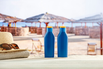 Wall Mural - Blue containers for sun tan lotion and sunscreen oils on a bright table with tropical  beach and a sea and clear sky background.