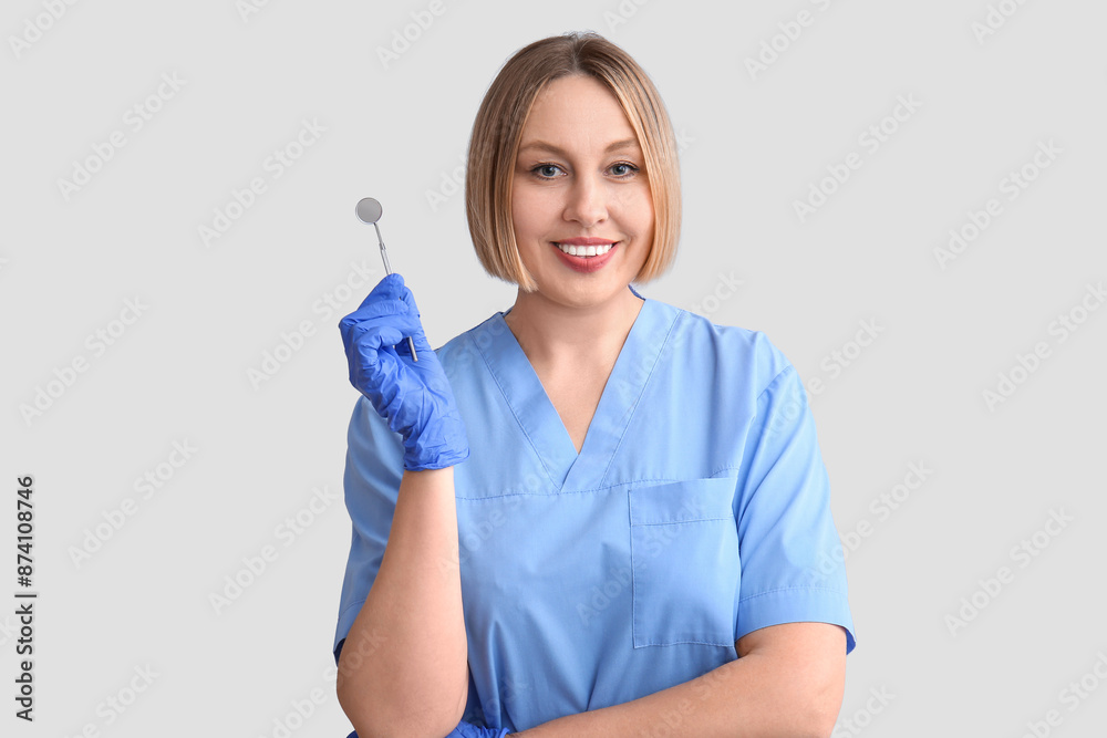 Female dentist with mirror on grey background