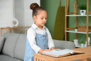 Wall Mural - Cute little girl reading Holy Bible at home