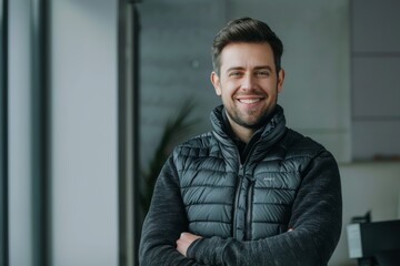 Wall Mural - Portrait of a glad man in his 30s dressed in a thermal insulation vest on sophisticated corporate office background