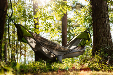 A green hammock hangs among the trees by the lake. A young girl is resting outdoors in a hammock. Picnic. Summer outdoor recreation with an overnight stay. Summer background