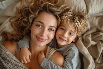 Top view of a happy mother and son laying on bed, hugging each other laughing together. love. Soft light, beige and brown tones.