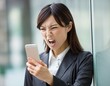 © black swamp - スマートフォンを見て怒る、びっくりするオフィス街のビジネスウーマン。