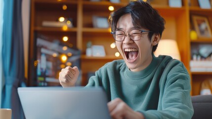 Poster - A young man is sitting in front of a laptop, laughing and celebrating