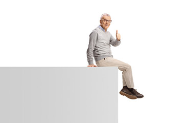 Wall Mural - Elderly man sitting on a wall and gesturing thumbs up