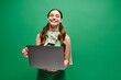 © LIGHTFIELD STUDIOS - A woman in her 20s holding a laptop in front of a vibrant green background, exuding digital empowerment and connection.