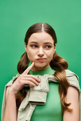 Wall Mural - A stylish young woman in her 20s pointing at cheek in a studio setting, wearing a striking green sweater.