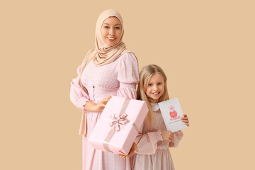 Canvas Print - Beautiful young Muslim woman holding gift box and her cute little daughter with greeting card on beige background