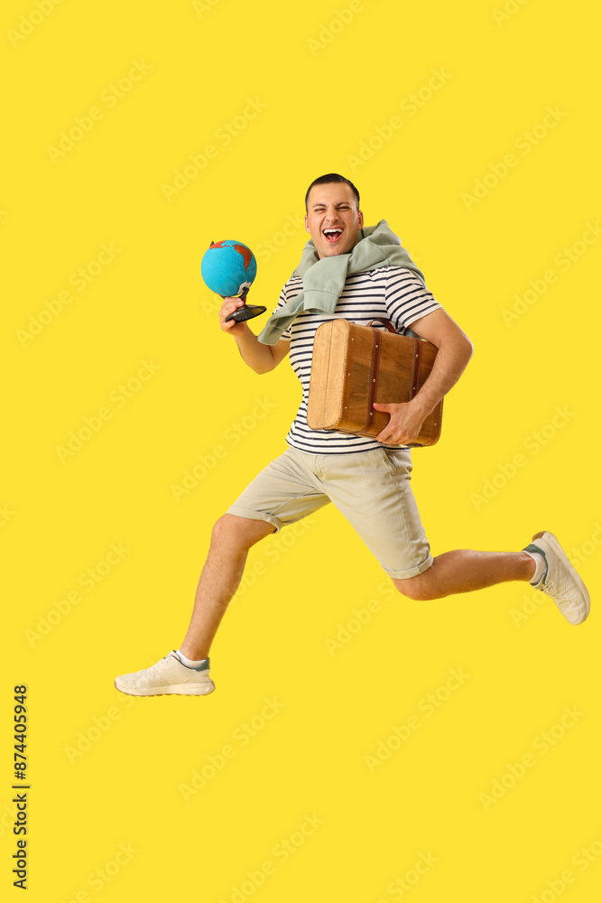 Male tourist with globe and suitcase jumping on yellow background