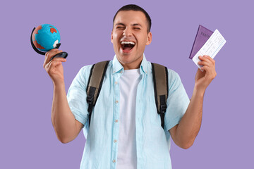 Wall Mural - Happy male tourist with globe and passport on lilac background