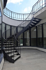 Exterior black steel spiral staircase by white concrete wall in Martvili canyon, Georgia. stairway to heaven with iron railings