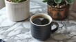 © fivan - A cup of dark roast coffee in a matte black mug on a marble countertop, with a small pot of succulents nearby