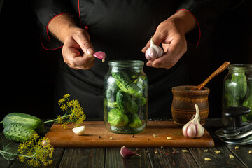 Wall Mural - A man adds garlic to a jar of cucumbers before preserving them with spices. The concept of pickling vegetables in the kitchen at home