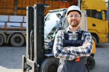 Wall Mural - forklift driver in protective vest and forklift standing at warehouse of freight forwarding company, smiling