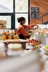 Wall Mural - African american merchant putting boxes of freshly harvested produce on shelves in environmentally friendly store. Female storekeeper preparing for an event supporting zero waste sustainable lifestyle