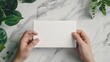© Ziyan - Hand holding greeting card mockup on clean background. White empty paper for text. Invitation, letter, gift, certificate template