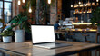 © chekart - A mockup of a stylish laptop in a trendy restaurant or cafe. There is an open laptop on a wooden table in the restaurant. The table is surrounded by potted plants