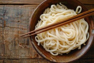 Poster - Overhead shot of a rustic bowl filled with udon noodles and chopsticks, resting on a wooden surface with copy space