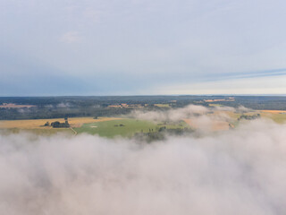 Wall Mural - Soft white fog covering the rural summer landscape of Latvia countryside. Aerial photography of mist clouds.