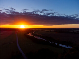 Wall Mural - A beautiful river flowing through the Latvia countryside during summer sunrise. Natural morning scenery from the air.