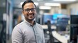 © Art Genie - Enthusiastic male IT professional in a casual shirt, smiling confidently at the camera, surrounded by computers and servers in an office, highlighting technical expertise