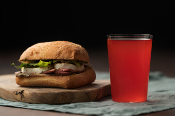 Wall Mural - Roast beef and mozzarella sandwich with ciabatta bun on olive board with red lemonade