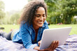© peopleimages.com - Tablet, nature and woman relaxing on blanket with smile for email on mortgage loan approval. Happy, digital technology and female person with research on finance investment online in outdoor park.