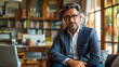 © paramee - Confident middle-aged man in a suit and glasses sitting in a cozy, well-lit home office