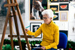 © ADDICTIVE STOCK - Elderly woman painting on canvas in artistically decorated room