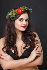 Wall Mural - Happy young woman with floral head wreath looking at camera while standing against black background