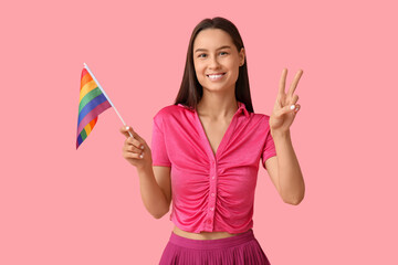 Wall Mural - Beautiful young woman with LGBT flag showing victory gesture on pink background